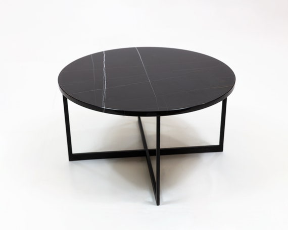 Mesa de centro redonda, realizada en metal acabado negro mate. Tapa de  piedra artificial acabado mármol blanco veteado.