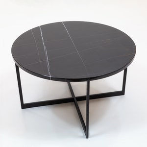 Könnte beinhalten: Ein runder Couchtisch aus schwarzem Marmor mit einem schwarzen Metallgestell. Der Tisch hat ein schlichtes, modernes Design.