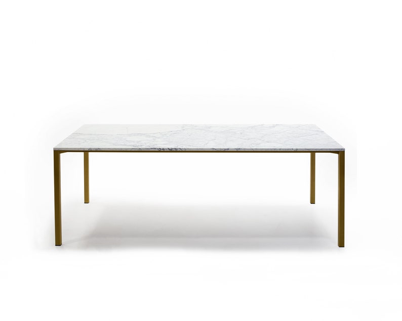 Puede incluir: Una mesa de comedor rectangular con tapa de m&aacute;rmol blanco y patas de metal dorado.