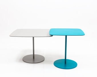 Op de afbeelding: Twee vierkante tafels met afgeronde hoeken. De tafel links heeft een grijs blad en een grijs onderstel. De tafel rechts heeft een tealblauw blad en een tealblauw onderstel.