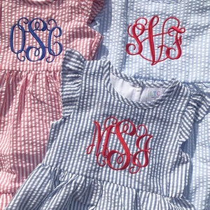 May include: Three girls' dresses with different colored stripes and embroidered monograms. The dresses are red and white striped, blue and white striped, and light blue and white striped. The monograms are in red and blue thread.