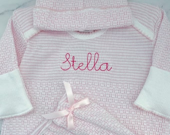 May include: A light pink and white waffle-knit long-sleeve shirt and matching hat set. The shirt features the name Stella embroidered in pink cursive script across the chest, white sleeve cuffs, and a small pink satin ribbon bow on the front.