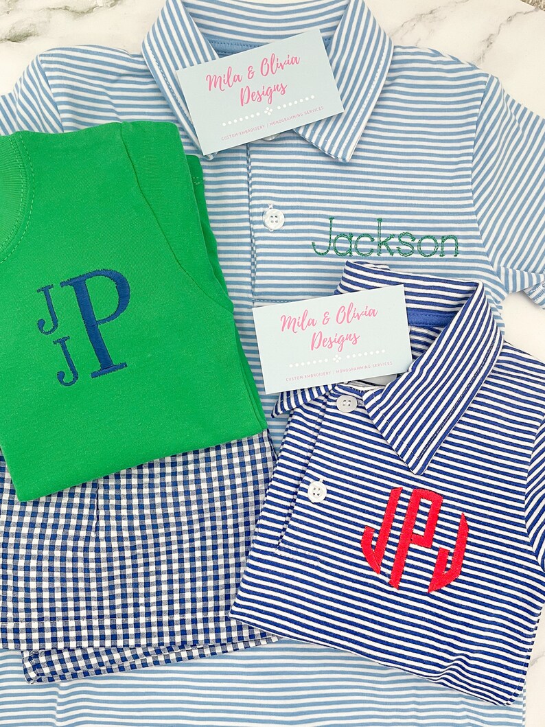 May include: A green t-shirt with a dark blue embroidered monogram, a light blue and white striped polo shirt with the green embroidered name Jackson, and a navy and white striped polo shirt with a red embroidered monogram, plus two business cards.