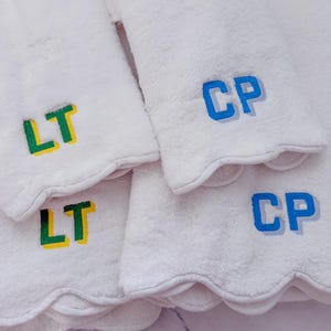 May include: White, scalloped-edge towels embroidered with initials. Two towels display "LT" in green and yellow, while two others feature "CP" in blue. The towels are fluffy and appear to be made of a soft material.