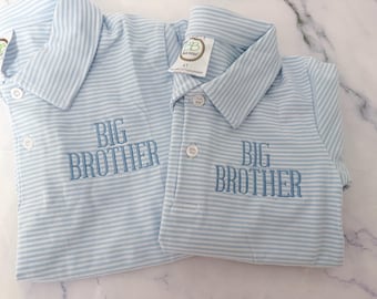 May include: Two light blue and white striped shirts with the embroidered text "BIG BROTHER". The shirts have a collared neckline and button closures. One shirt has a tag that reads "4T".