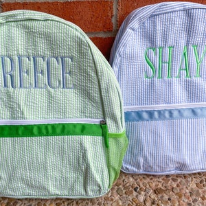 May include: Two personalized green and blue backpacks with the names Reece and Shay embroidered on them.