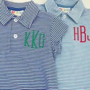May include: Two short-sleeved polo shirts featuring white and blue horizontal stripes. The left shirt is dark blue with green embroidered KKG initials. The right shirt is light blue with red embroidered HBJ initials. Both feature white buttons and Tell Bean labels.