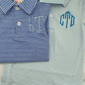 May include: Two short-sleeved polo shirts with horizontal stripes. One shirt is dark blue and white with a light blue embroidered monogram. The other is light blue and white with a dark blue embroidered monogram. A business card reads Mila & Olivia Designs.
