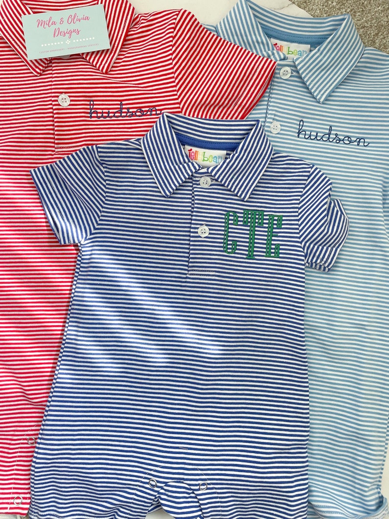May include: Three short-sleeved polo rompers featuring horizontal stripes in red, light blue, and dark blue. Each garment has a collar, a button placket, and snap closures at the bottom. The red and light blue rompers feature the embroidered name hudson.