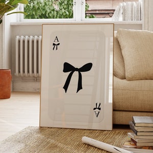 Puede incluir: Una tarjeta blanca con un lazo negro y la letra A en ella. La tarjeta está enmarcada y colgada en una pared.