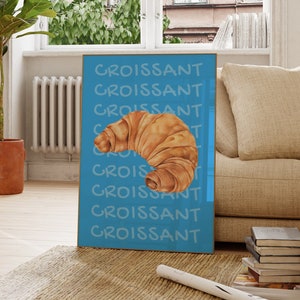 Puede incluir: Un póster azul con la palabra "Croissant" repetida varias veces en texto blanco. Un croissant marrón está centrado en el póster.