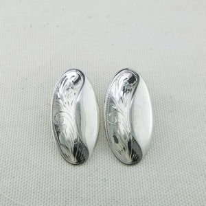 May include: A pair of silver oval-shaped earrings with a floral design etched into the surface.