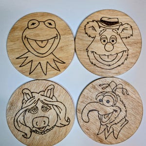 Può includere: Quattro sottobicchieri in legno con i personaggi dei Muppet: Kermit la Rana, Fozzie l'Orso, Miss Piggy e Gonzo. Ogni sottobicchiere presenta un disegno dettagliato del volto del personaggio, realizzato a pirografia. I sottobicchieri sono rotondi.