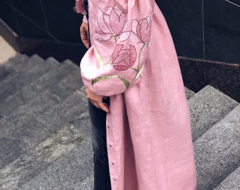 以下が含まれることがあります： 袖に刺繍された花柄のディテールが施された、長いピンクのリネンワンピース。ワンピースはフロントにボタン留めがあり、ゆったりとしたフィット感です。