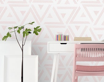 May include: A white desk with a pink chair and a white bedside table with two drawers. The wall behind the desk is covered in a pink and white geometric wallpaper with a pattern of triangles.
