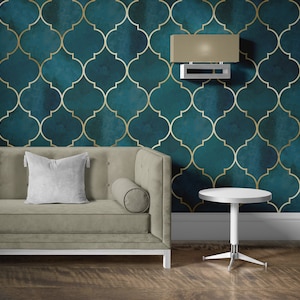 May include: A light gray couch with a white pillow and a round gray bolster. The couch is in front of a teal and gold patterned wall with a light fixture above. A small white round table with a silver base sits in front of the couch.