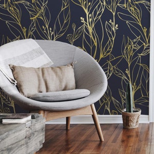 Puede incluir: Un sillón gris con una base de madera marrón se encuentra frente a una pared azul oscuro con un patrón de hojas doradas. Un pequeño cactus en maceta se encuentra en el suelo junto a la silla.