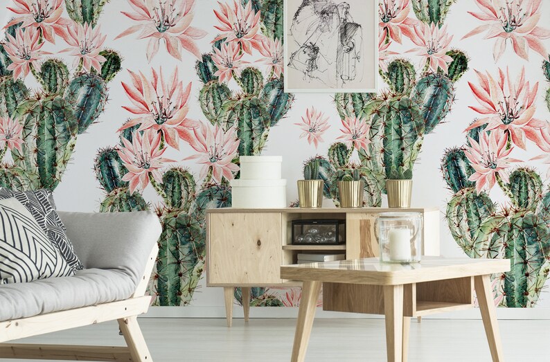 May include: A living room interior with a light grey sofa and a wooden coffee table. The wall is covered in a wallpaper with a repeating pattern of pink cactus flowers and green cacti.