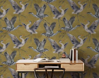 May include: A mustard yellow wallpaper with a repeating pattern of gray cranes in flight. A wooden desk with a drawer and a chair are in front of the wallpaper.