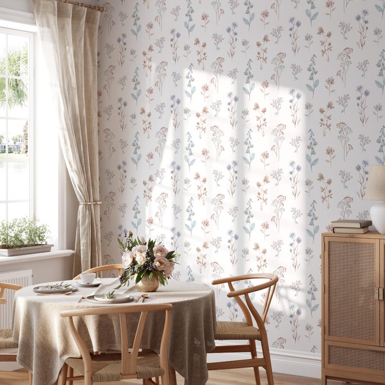 K&ouml;nnte beinhalten: Ein Esszimmer mit einem runden Tisch, der f&uuml;r eine Mahlzeit gedeckt ist, Holzst&uuml;hlen und einem Blumenarrangement. Die W&auml;nde sind mit Tapeten mit zarten blauen, braunen und rosa Blumen geschm&uuml;ckt. Ein Fenster mit beigen Vorh&auml;ngen l&auml;sst nat&uuml;rliches Licht herein.