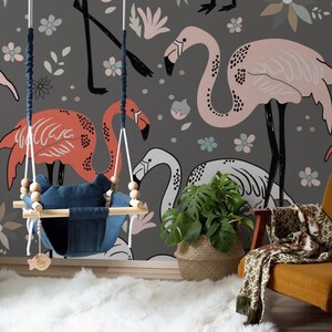 May include: A nursery room with a gray wall mural featuring pink, red, and white flamingos with floral accents. A wooden baby swing with a blue fabric seat hangs in front of the mural. A potted plant and a chair with a throw blanket are in the foreground.