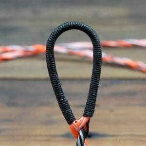 May include: A close-up shot of a black loop with a textured surface, attached to a rope with orange, white, and black strands. The loop is the focal point, with the rope blurred in the background.