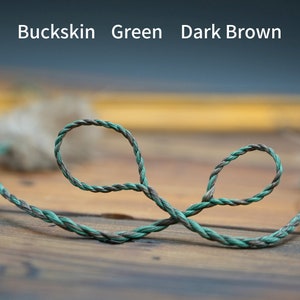 Può includere: Primo piano di una corda ritorta nei toni del verde e marrone scuro, disposta a forma di otto. Il testo "Buckskin Green Dark Brown" è visibile nella parte superiore dell'immagine, su uno sfondo sfocato.