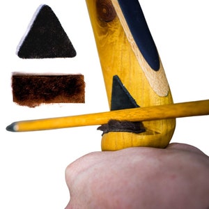 May include: Close-up of a wooden archery bow with a yellow shaft and black accents. The bow is held by a hand. Two separate pieces of black and brown felt are shown above the bow.