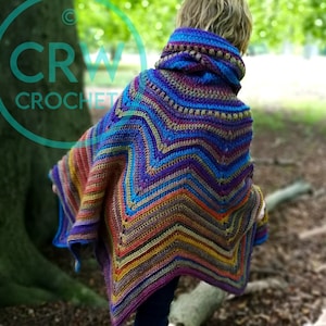 May include: A colorful crocheted poncho with a hood, featuring a chevron pattern in shades of blue, purple, orange, and brown. The poncho is worn by a person in a forest setting.