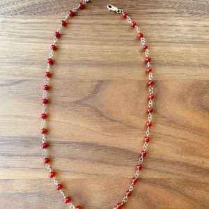 May include: A silver chain necklace with small red beads.