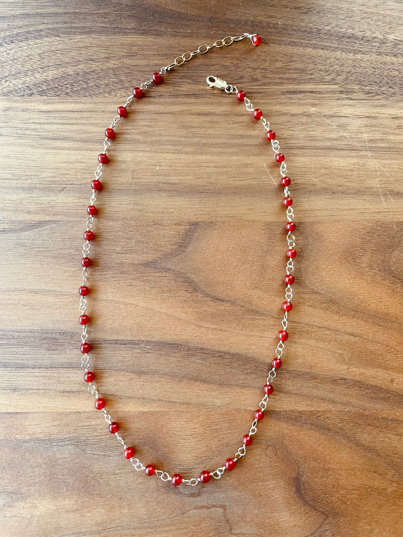 May include: A silver chain necklace with small red beads.