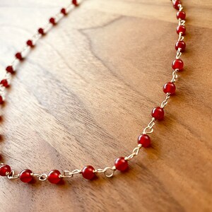 May include: A gold chain necklace with small, round, red carnelian beads.
