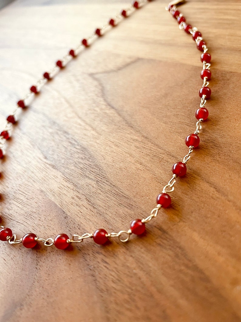 May include: A gold chain necklace with small, round, red carnelian beads.