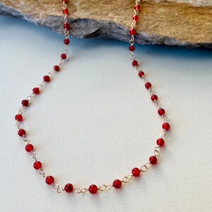 May include: A red carnelian gemstone necklace with a gold chain. The necklace is made of small, round beads and is approximately 18 inches long.