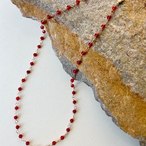 May include: A delicate gold chain necklace with small, red gemstone beads.