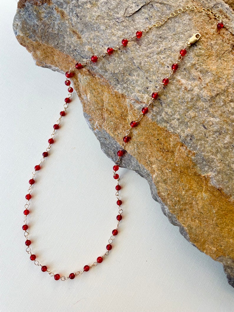 May include: A delicate gold chain necklace with small, red gemstone beads.