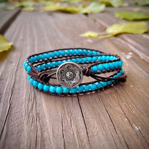 May include: A turquoise and brown leather wrap bracelet with a silver charm featuring a floral design.
