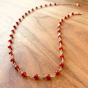 May include: A red carnelian gemstone necklace with gold chain links. The necklace is on a wooden surface.