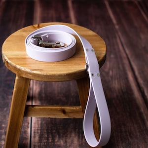 Peut inclure: Une laisse de chien en cuir lavande avec une boucle argent&eacute;e, enroul&eacute;e sur un tabouret en bois.