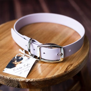 Peut inclure: Un collier pour chien de couleur lavande avec une boucle argent&eacute;e et un anneau en D argent&eacute;. Le collier est pos&eacute; sur une surface en bois avec une petite &eacute;tiquette qui indique "Firma Cubi Handmade Pet Collars Est. 2018".