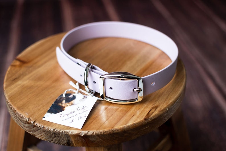Peut inclure: Un collier pour chien de couleur lavande avec une boucle argent&eacute;e et un anneau en D argent&eacute;. Le collier est pos&eacute; sur une surface en bois avec une petite &eacute;tiquette qui indique "Firma Cubi Handmade Pet Collars Est. 2018".
