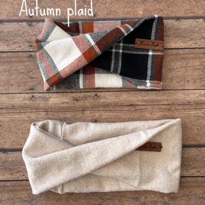May include: Two fabric headbands. The top headband features an autumn plaid pattern in white, black, and burnt orange with a brown leather tag. The bottom headband is a solid light beige with a herringbone texture and a matching brown leather tag.