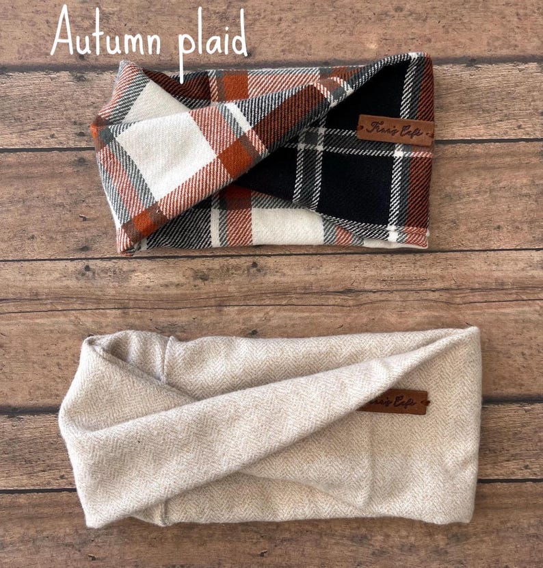 May include: Two fabric headbands. The top headband features an autumn plaid pattern in white, black, and burnt orange with a brown leather tag. The bottom headband is a solid light beige with a herringbone texture and a matching brown leather tag.