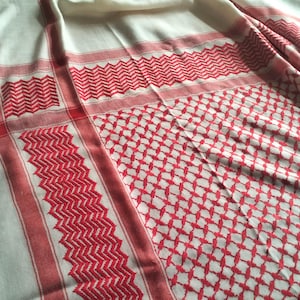 Puede incluir: Una tela con un patrón blanco y rojo con un diseño tradicional. La tela está doblada y muestra los intrincados detalles del patrón.