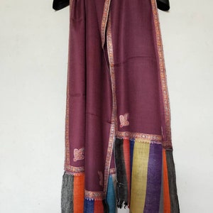 May include: A maroon shawl with a colorful striped border and embroidered floral designs. The shawl is made of soft, luxurious fabric and is perfect for adding a touch of elegance to any outfit.