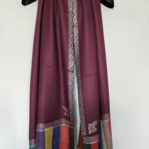May include: A maroon shawl with a colorful striped border and intricate floral embroidery along the edges. The shawl is made of soft, luxurious fabric and is perfect for adding a touch of elegance to any outfit.