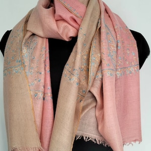 May include: A pink and beige shawl with a paisley pattern and a fringed edge. The shawl is made of soft, lightweight fabric and is perfect for adding a touch of elegance to any outfit.