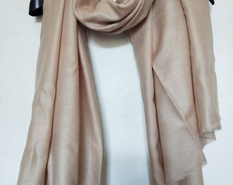 May include: A light beige pashmina shawl made of soft cashmere. The shawl is draped over a hanger and has a smooth, silky texture.