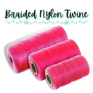 Könnte beinhalten: Drei Rollen leuchtend rosa geflochtenes Nylongarn. Die Rollen sind diagonal angeordnet, die größte hinten und die kleinste vorne. Der Text "Braided Nylon Twine" befindet sich über den Rollen in einer Schriftart.