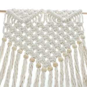 May include: A white macrame wall hanging with wooden beads. The hanging is made of a thick, knotted rope and has a diamond pattern. The beads are evenly spaced along the bottom edge of the hanging.